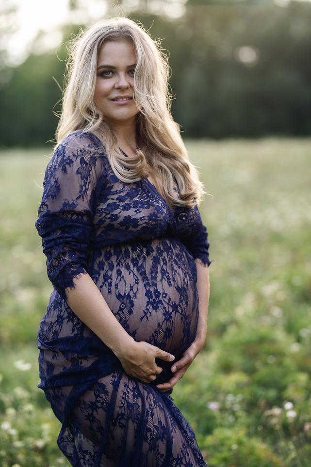 Těhotná žena v modrých krajkových šatech uprostřed louky